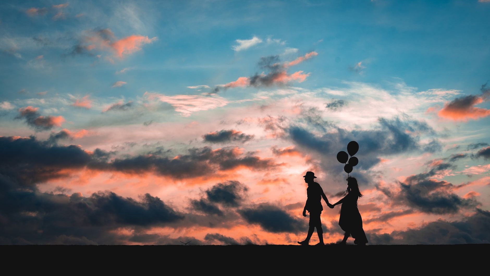 A couple holding balloons walks against a vibrant sunset in Cartagena, Colombia.