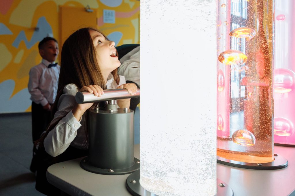 Children engage with interactive science exhibit featuring colorful liquids and lights.