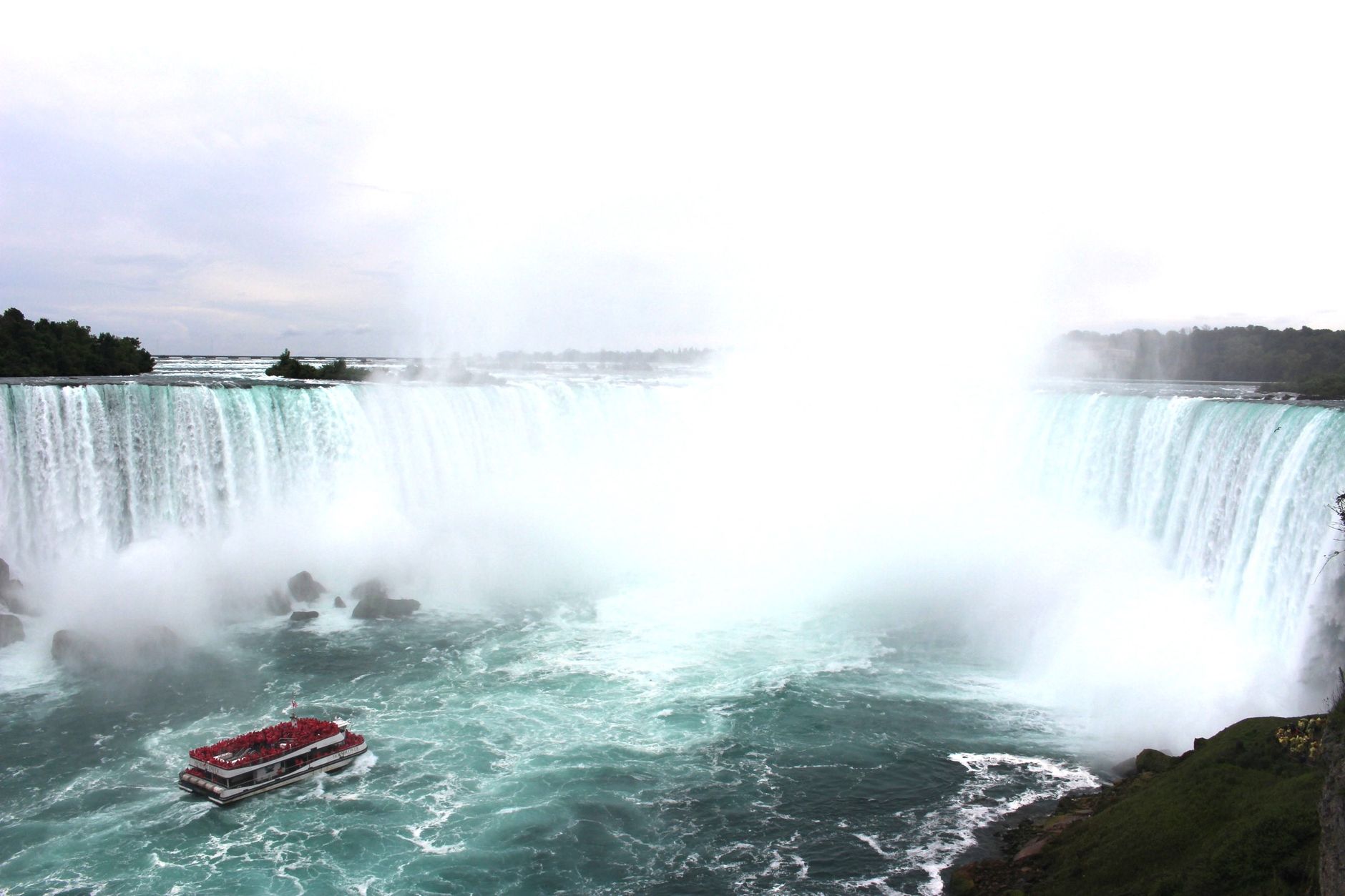 A breathtaking aerial view of Niagara Falls with a tour boat navigating the misty waters below.
