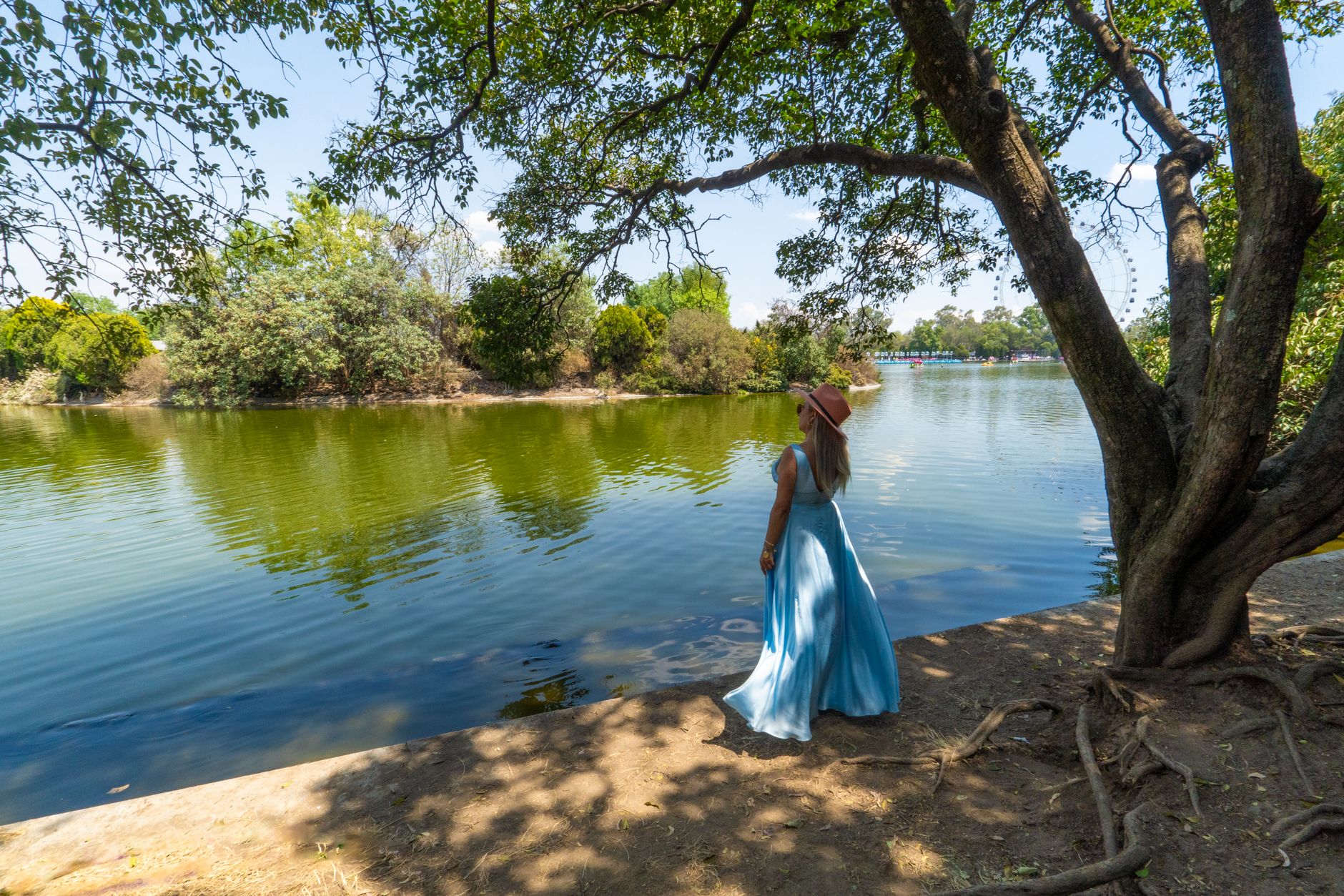 Woman in elegant dress enjoying a serene view by the lake in Chapultepec Park, Mexico City.