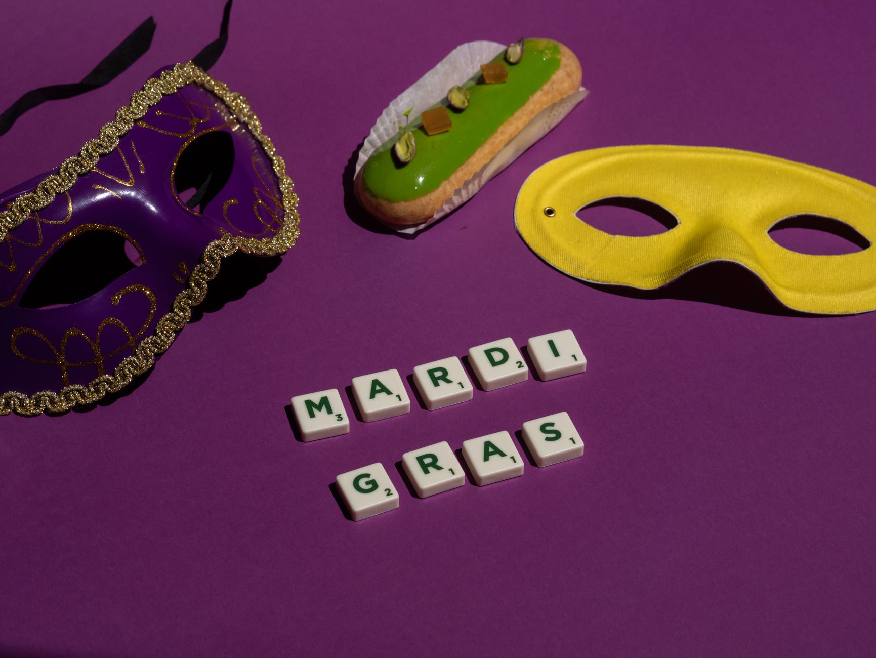Festive purple background with Mardi Gras masks and a green pastry, symbolizing celebration.