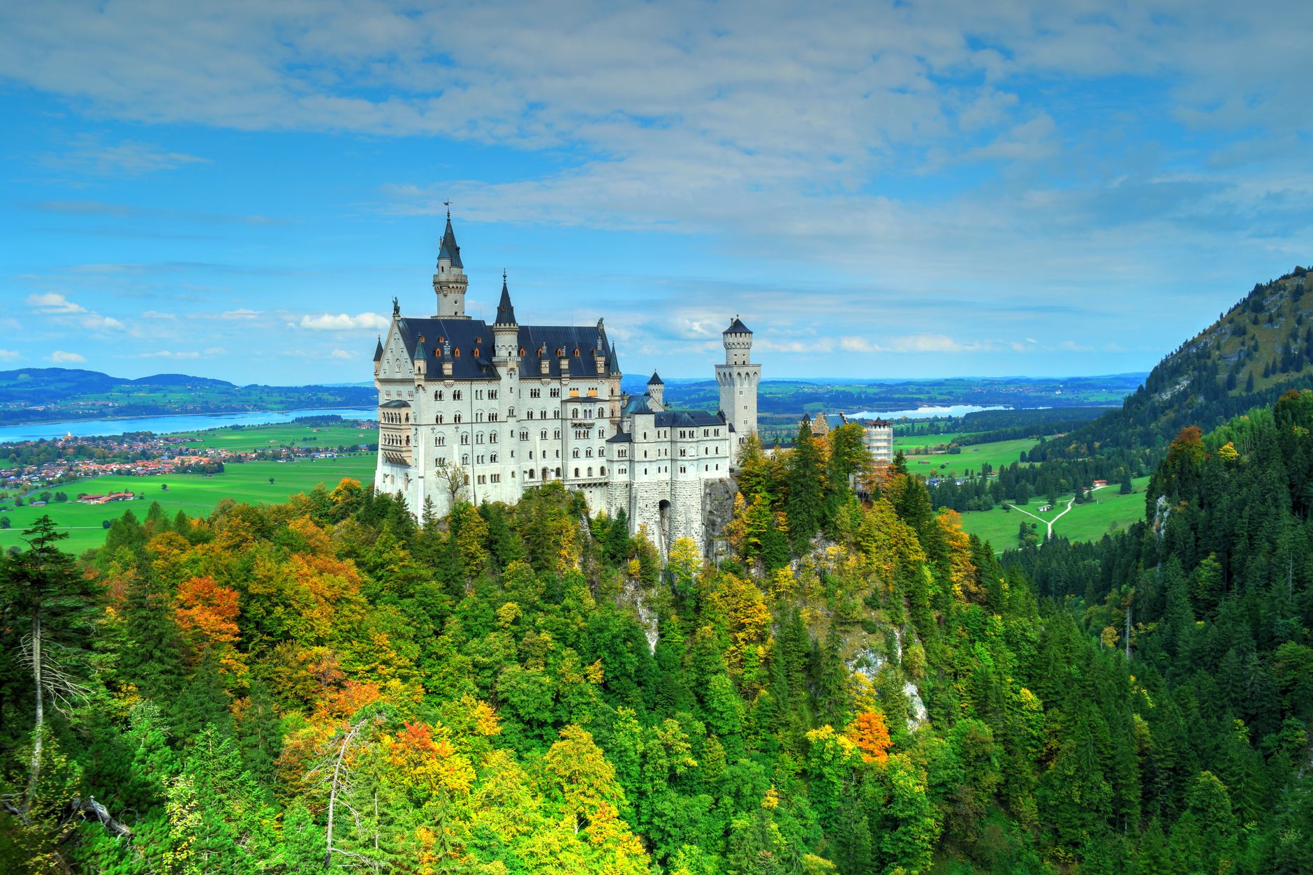 Aerial view of Neuschwanstein Castle amid vibrant autumn foliage with scenic landscape.