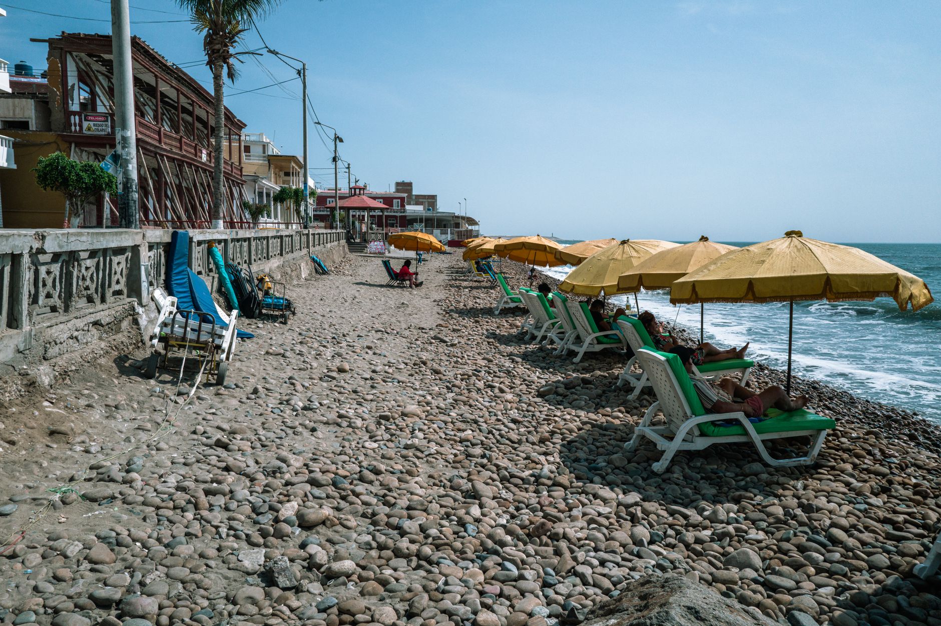 Sunbathers on a pebble beach with yellow umbrellas in Pacasmayo, Peru.