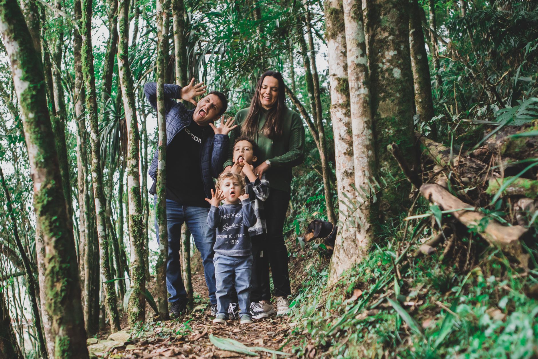 Playful family enjoying a silly moment amidst a vibrant green forest trail.