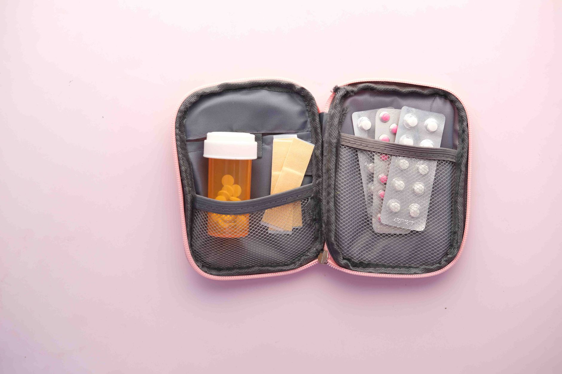 Open first aid kit with pill bottle, blister packs, and band-aids on a pastel background.