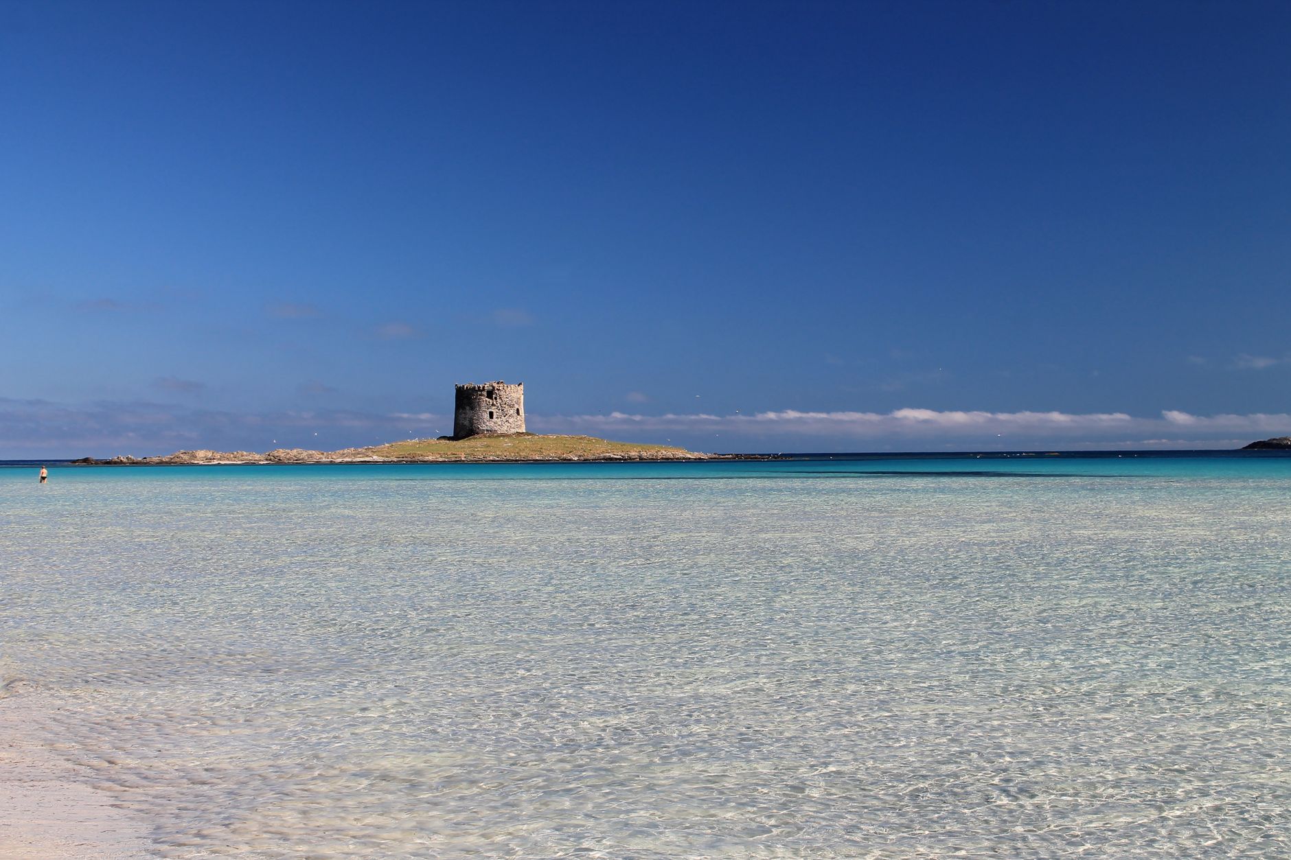 Panoramic view of Stintino Beach with azure waters and clear skies in Sardinia, Italy.