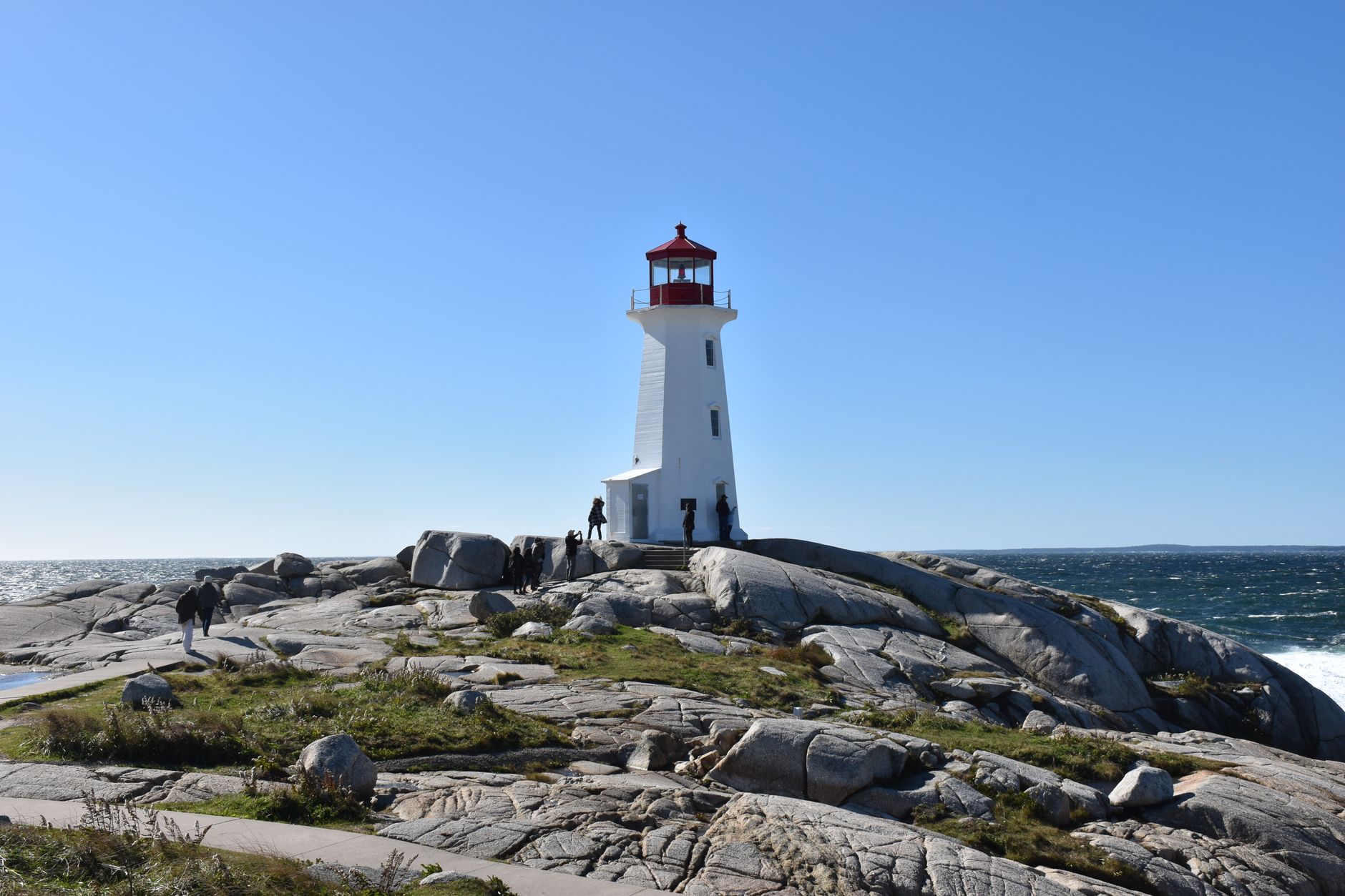 A stunning day view of the iconic Peggy's Cove Lighthouse surrounded by rocky terrain and ocean waves.