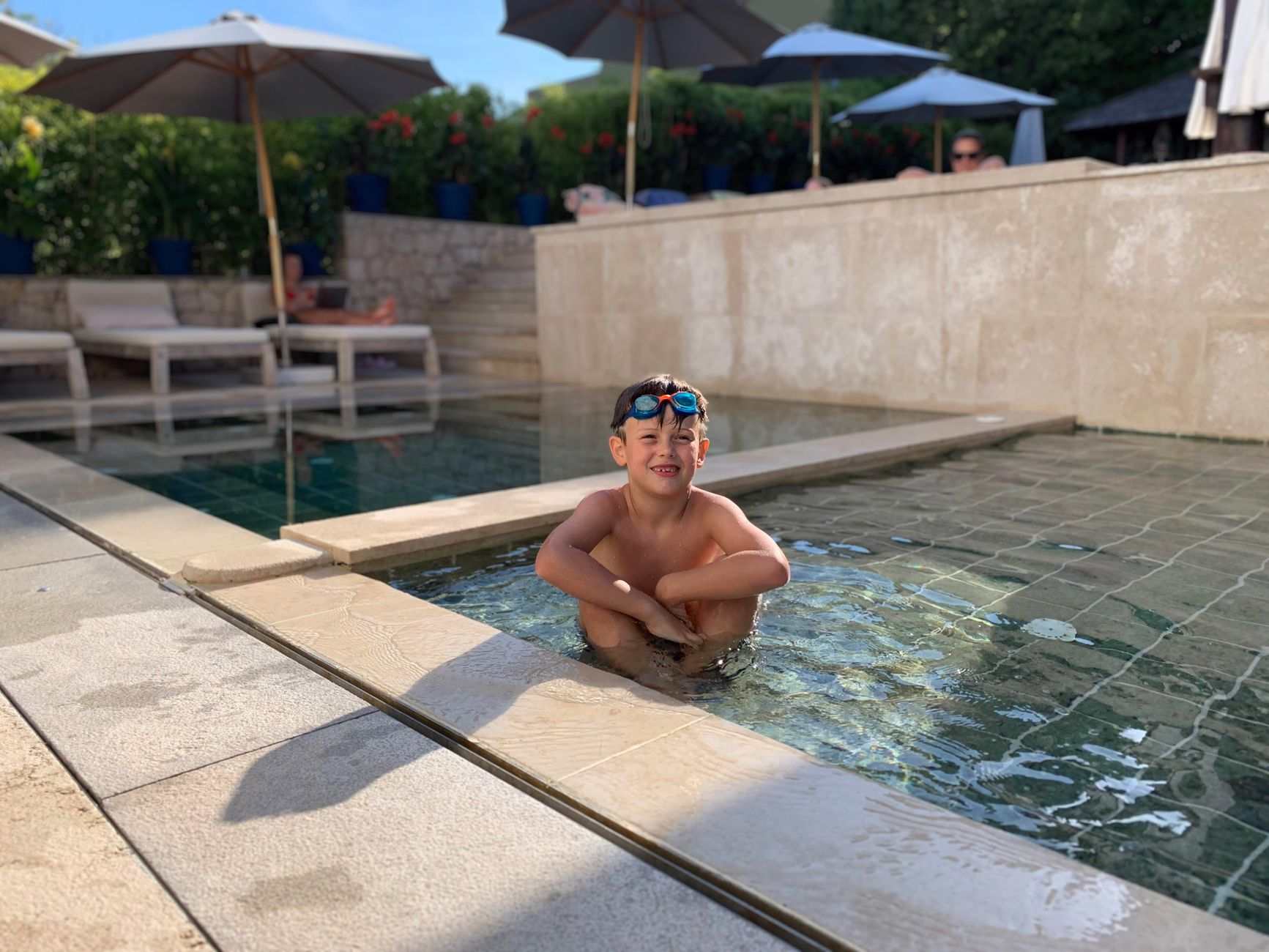 A child with goggles relaxes in a sunny outdoor pool in Nerezine, Croatia.