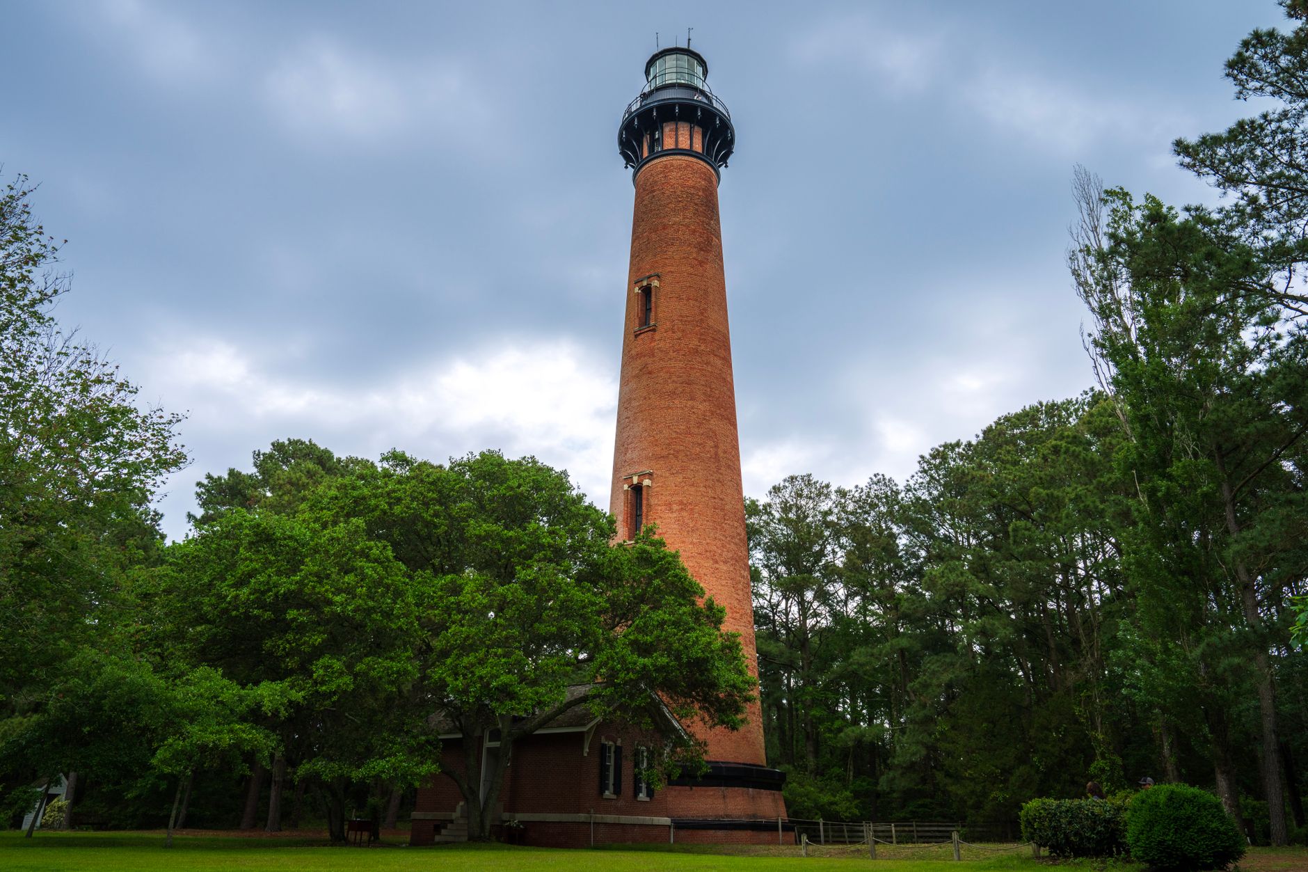 Beautiful view of Currituck Beach Lighthouse surrounded by lush trees on a cloudy day.