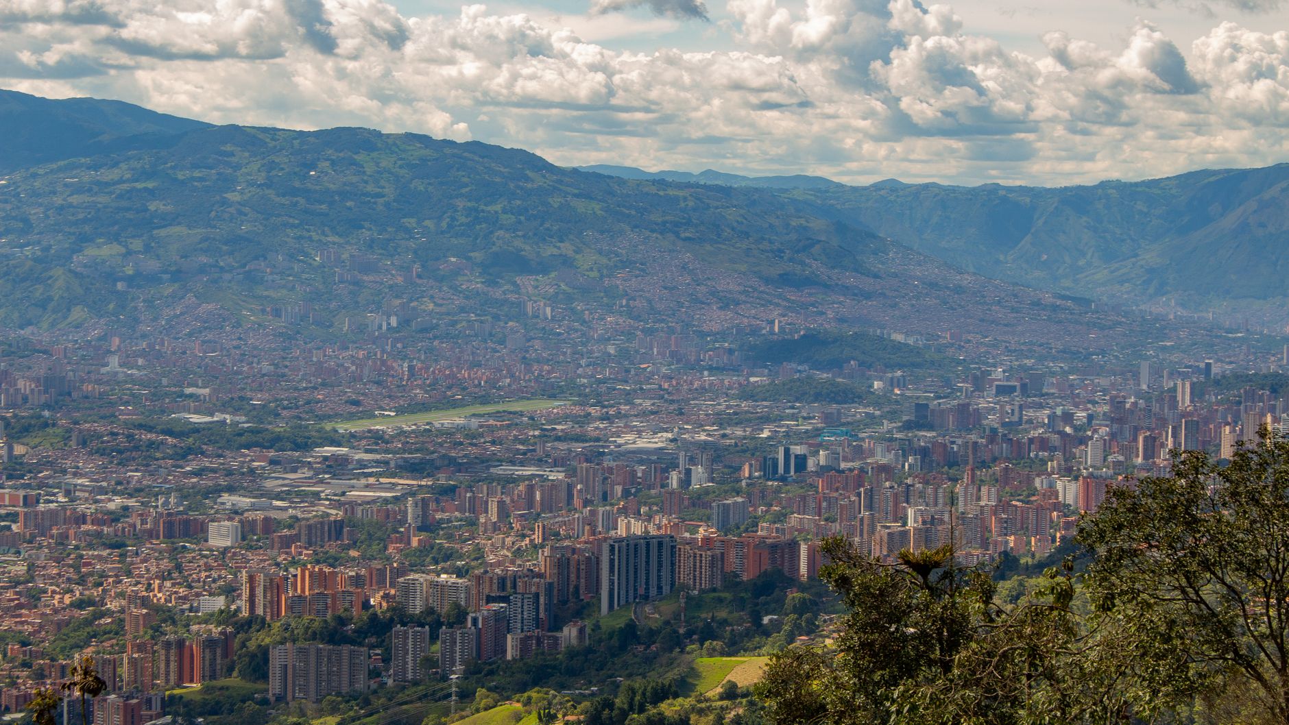 Breathtaking aerial view of Medellín, Colombia, surrounded by mountains under a cloudy sky.