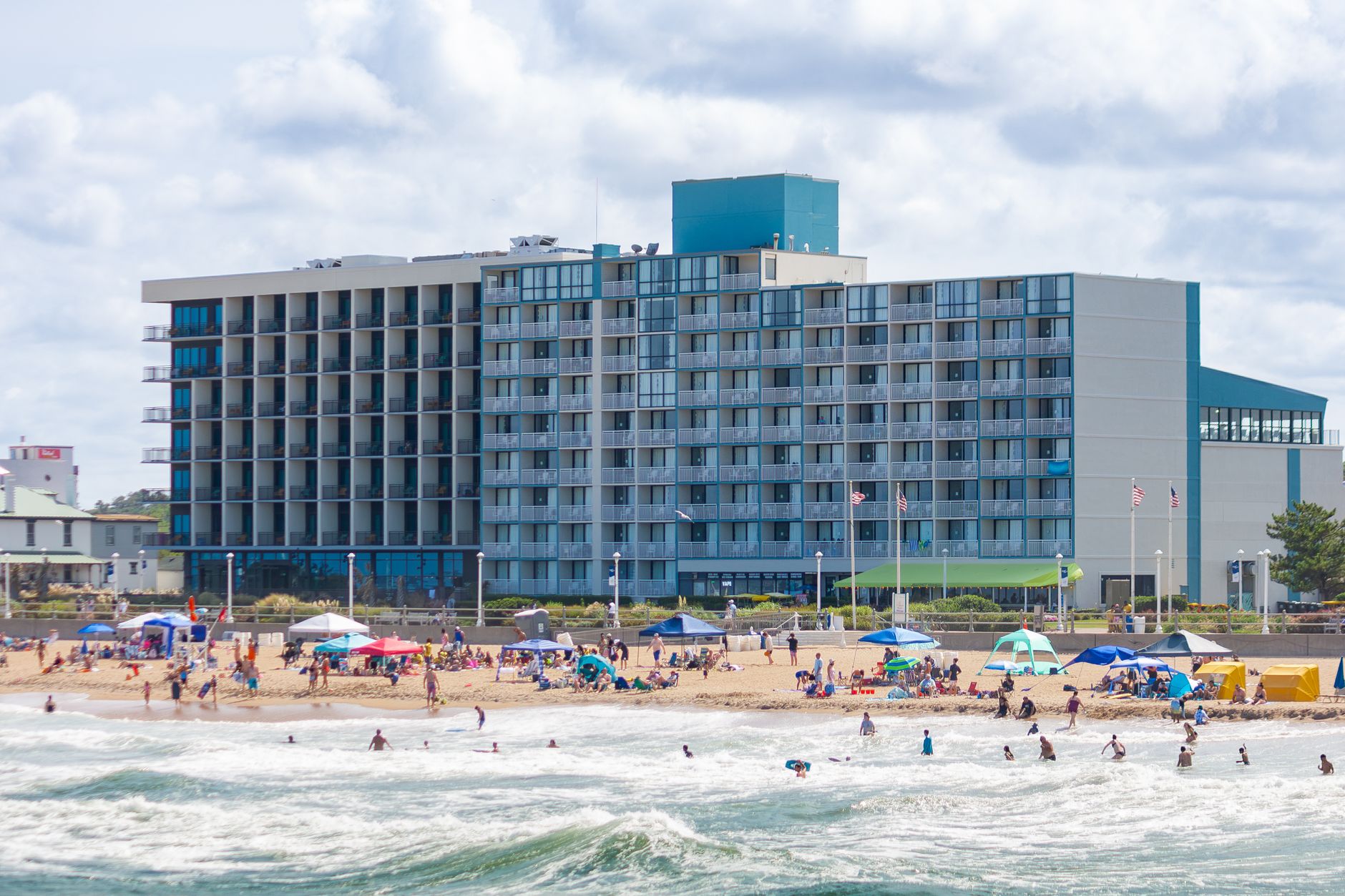 Lively summer day at Virginia Beach with people enjoying the sand and surf in front of a beachfront hotel.
